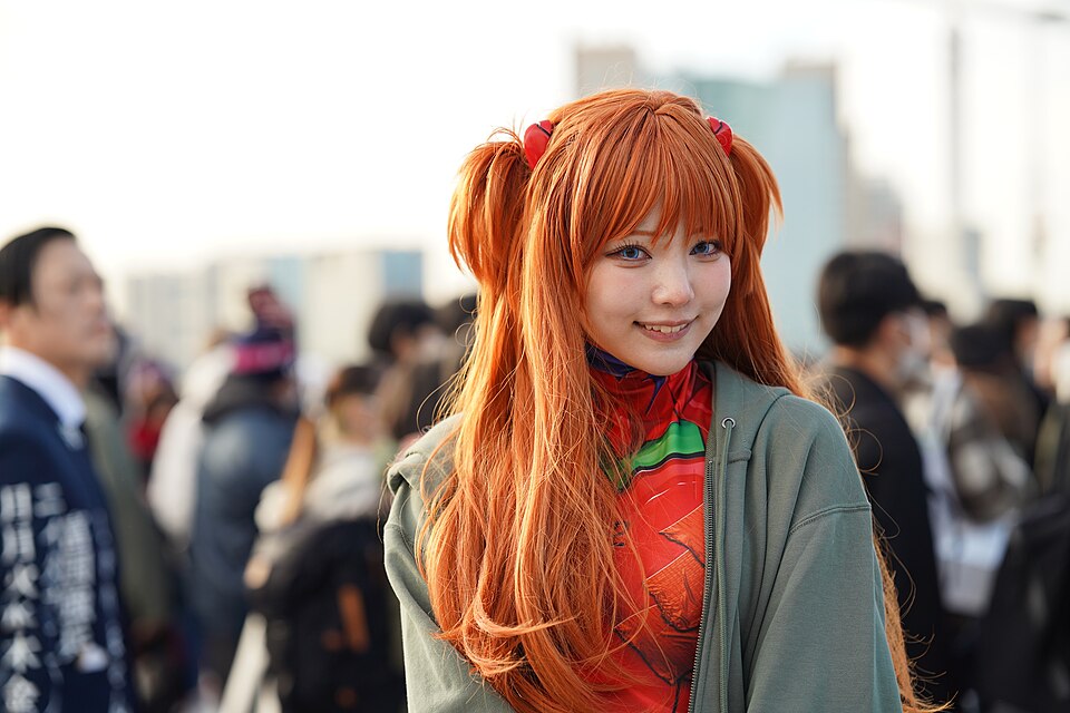 Cosplayer caracterizada como Asuka Langley Soryu (Evangelion), com cabelo ruivo e sorriso contido.