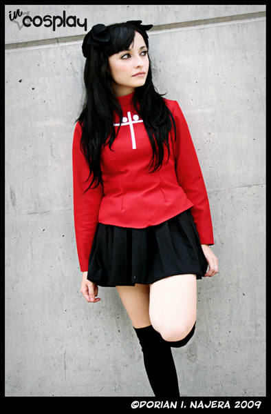 Cosplayer caracterizada como Rin Tohsaka (Fate/stay night), com roupa vermelha e expressão confiante.