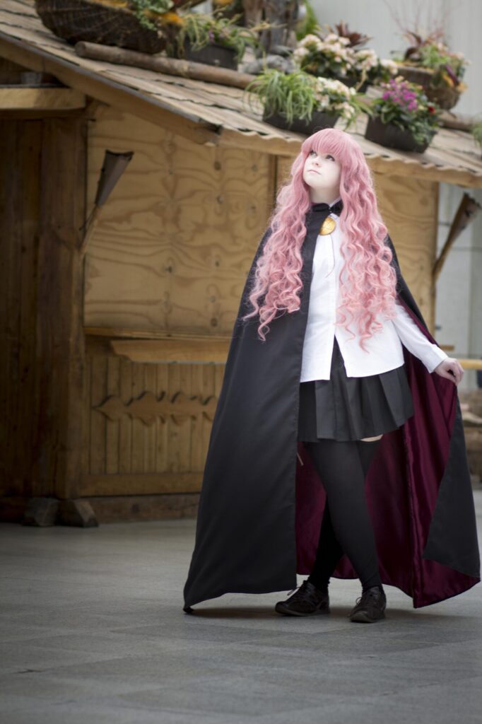 Cosplayer caracterizada como Louise (Zero no Tsukaima), com peruca rosa e uniforme, em pose dramática.